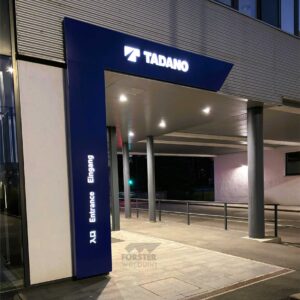 Beleuchteter Eingang mit Tadano-Logo bei Nacht.